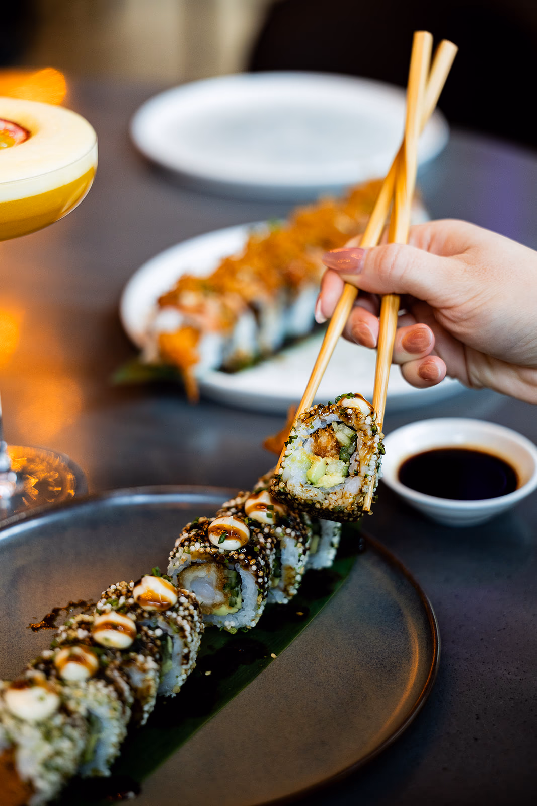 Hand met stokjes tilt een stuk sushi van het bord bij Graça